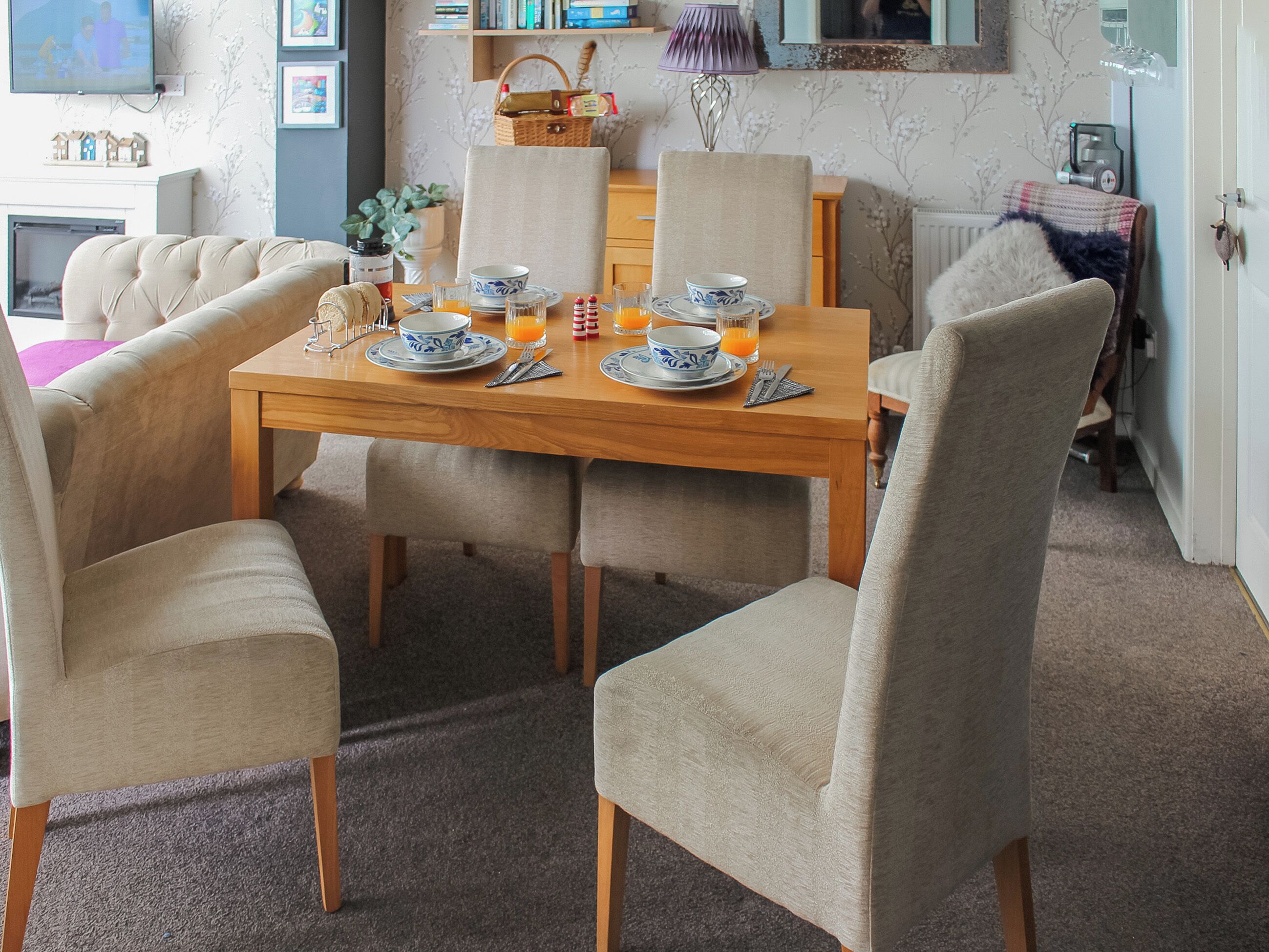 A dining area with a wooden table set for four, surrounded by upholstered chairs.