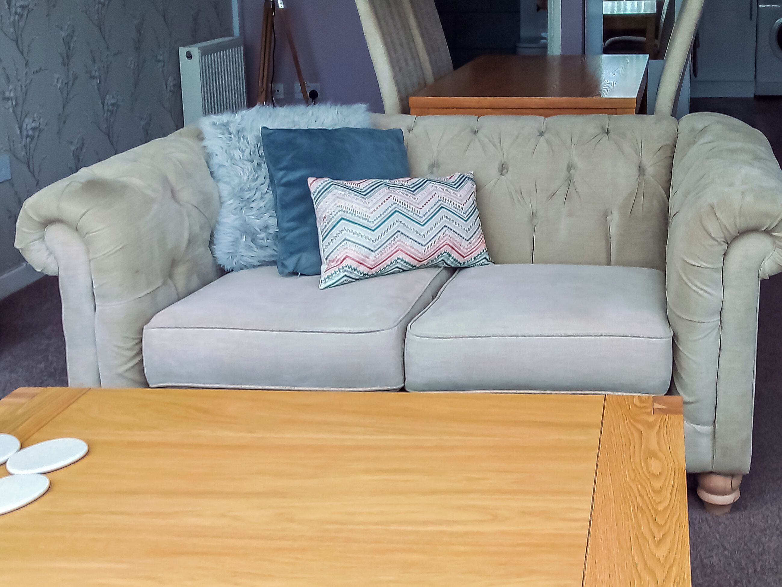 A beige tufted sofa with a patterned pillow and a wooden coffee table.