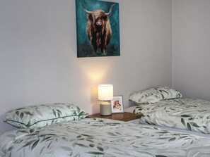 A bedroom with a bed featuring a leaf-patterned duvet, a bedside lamp, and a framed photo on the nightstand. - Sunrise Cottage - UK35813 (Llanddulas, near Llandudno)