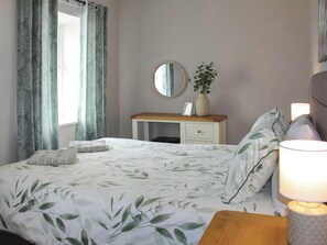 A bedroom with a bed, a bedside table, a nightstand, a dresser, a mirror, and a window with curtains. - Sunrise Cottage - UK35813 (Llanddulas, near Llandudno)