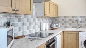 A modern kitchen with wooden cabinets, a microwave, a toaster, and a dishwasher. - Sunrise Cottage - UK35813 (Llanddulas, near Llandudno)