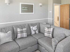 A grey sectional sofa with plaid cushions, a framed artwork of birds, and a wooden door in a neutral-toned room. - Sunrise Cottage - UK35813 (Llanddulas, near Llandudno)