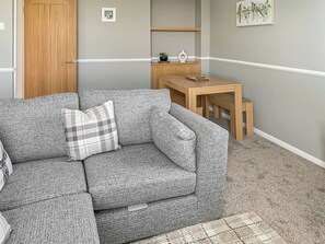A grey textured sofa with a plaid pillow, a wooden door, a small wooden table, and a framed bird painting on the wall. - Sunrise Cottage - UK35813 (Llanddulas, near Llandudno)