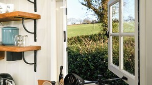 Una cucina con scaffali in legno, un bollitore e una finestra che si affaccia su un paesaggio verde.