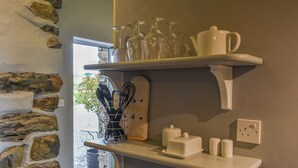 En køkkenhylde med glas, en ballonpisker holder og en kaffemaskine.