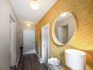 A hallway with a wooden textured wall, a round mirror, a white door, and a white lamp.