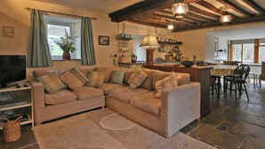Un salon chaleureux avec un canapé d’angle beige, un téléviseur et un coin repas comprenant une table et des chaises.