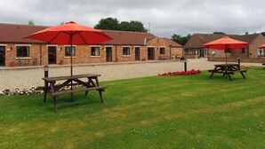 A courtyard with picnic tables and red umbrellas, surrounded by brick buildings with tiled roofs.