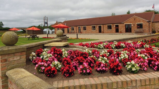 A brick building with a red-tiled roof, a flag, and a flower garden in front.