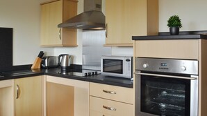 A modern kitchen with wooden cabinets, a stainless steel range hood, a microwave, and an oven.