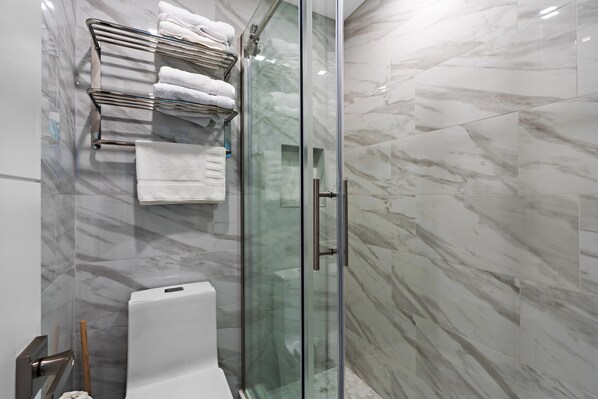 A modern bathroom with a glass shower enclosure, a white toilet, and a towel rack with folded towels.