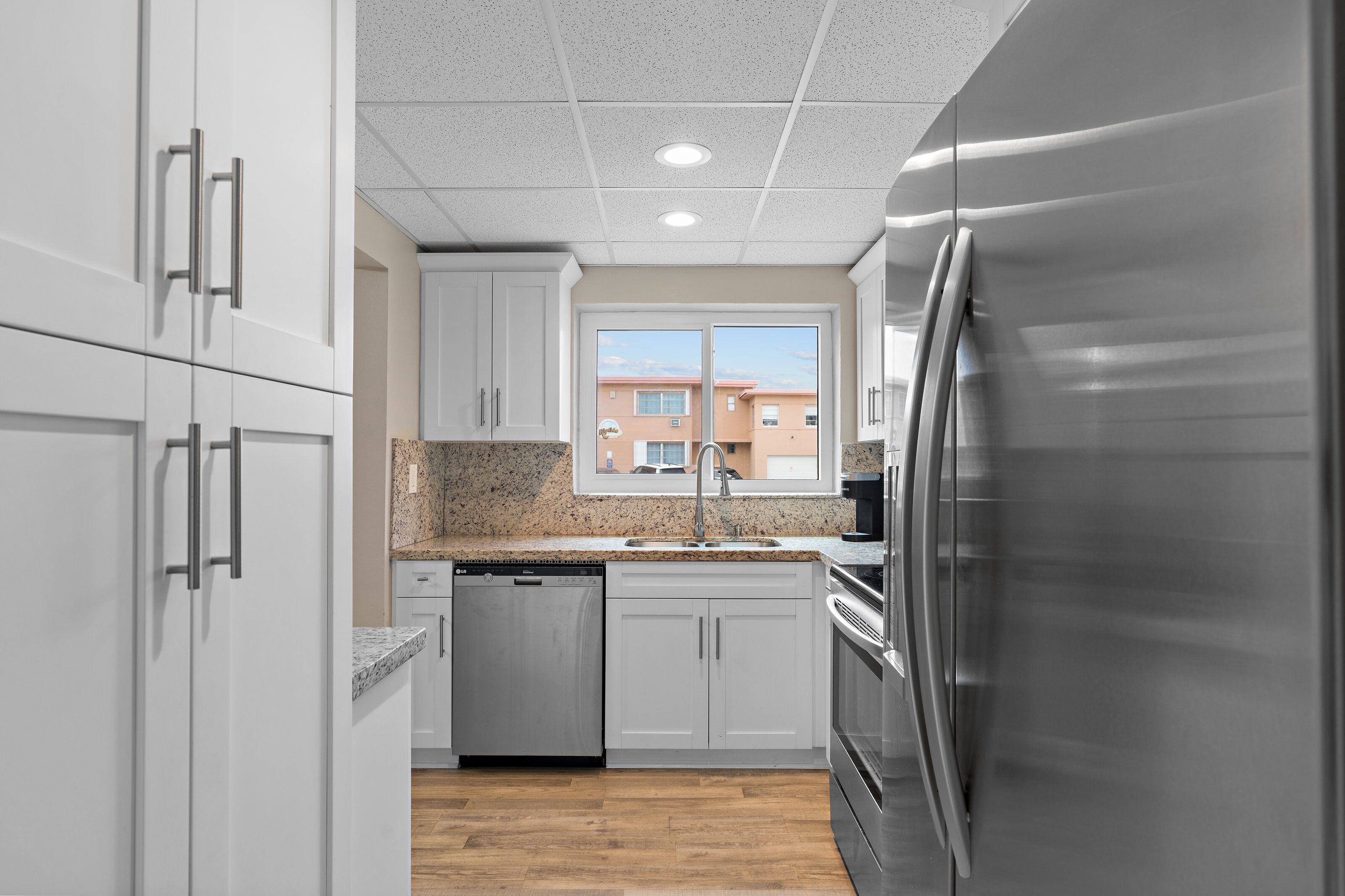 Una cocina moderna con gabinetes blancos, un refrigerador de acero inoxidable y una encimera de granito.