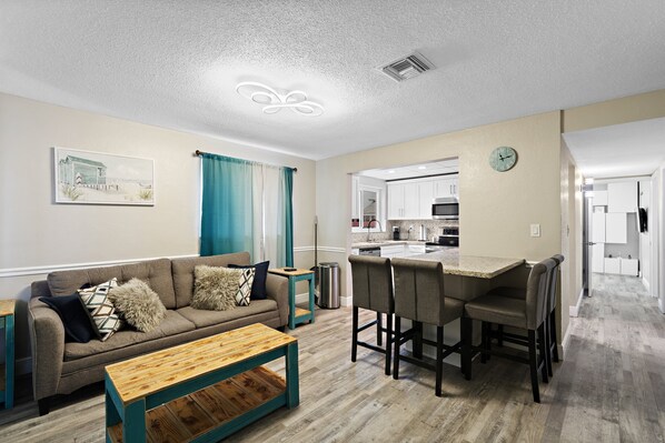 A modern living room with a sofa, coffee table, and a kitchen area with a dining set.