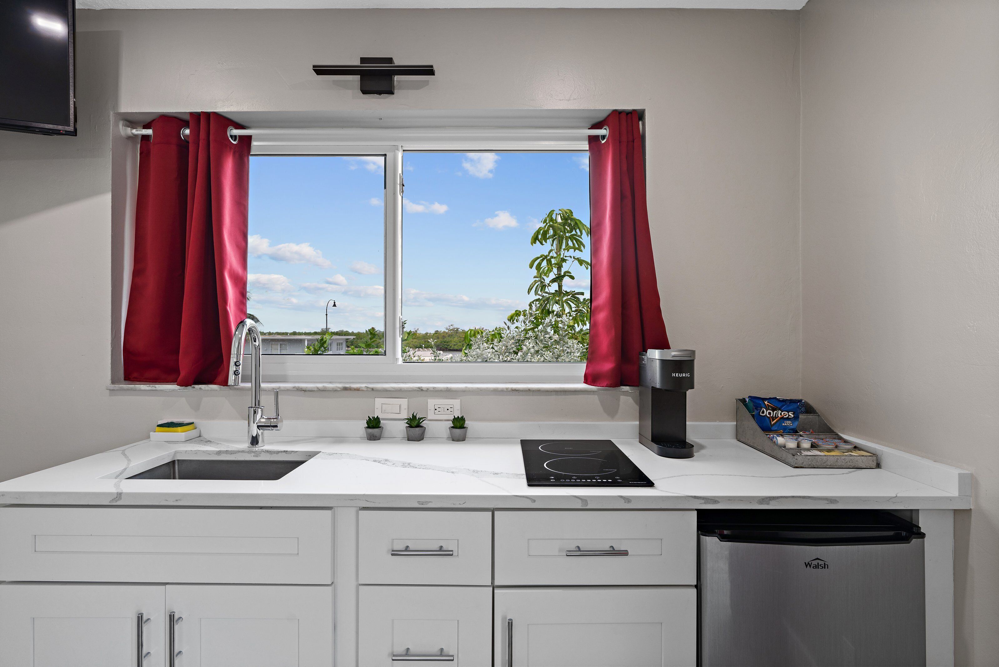 A modern kitchen with a sink, stove, and a window with red curtains.