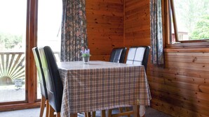 L’intérieur d’une cabane en bois, avec une table à manger, des chaises, un luminaire suspendu et des rideaux.