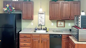Una cocina con armarios de madera, un refrigerador negro, lavavajillas y encimera de granito.