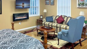 Una sala de estar bien iluminada con una cama, un sofá, un sillón y un televisor.