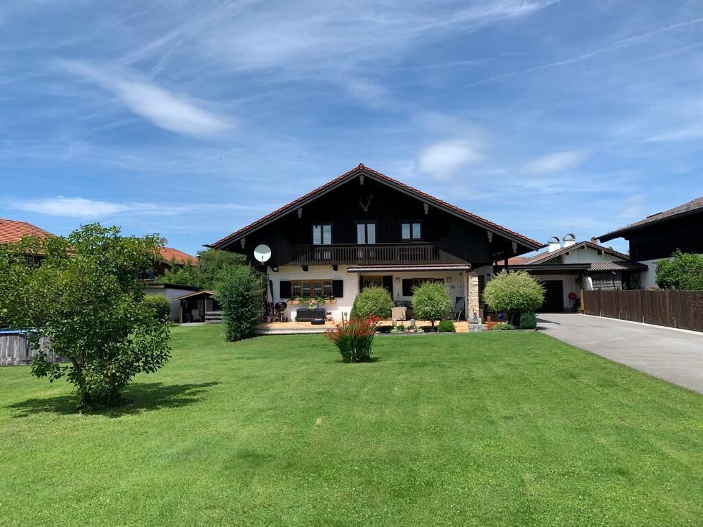 A large, two-story chalet with a prominent balcony, surrounded by a well-maintained lawn and several trees.