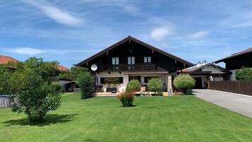 A large, two-story chalet with a prominent balcony, surrounded by a well-maintained lawn and several trees.