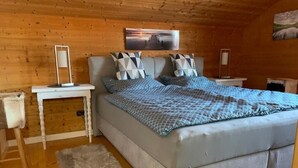 Un dormitorio acogedor con una cama grande, paredes de madera, una mesita de noche blanca y una alfombra mullida.