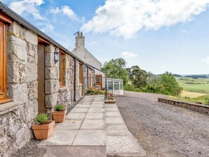 A stone building with a gravel pathway leading to a conservatory.
