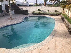 Piscina com borda curva, cercada por um muro de pedra e um deck revestido com azulejos.