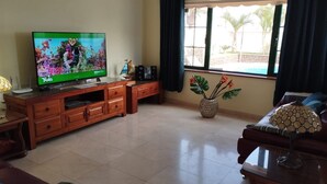 Un salon comprenant un téléviseur, un meuble de rangement en bois, un canapé, une table basse et une fenêtre avec des rideaux.