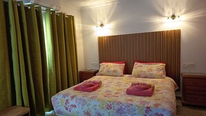 Une chambre à coucher avec une couvre-lit à motifs floraux, deux tables de chevet, une tête de lit en bois et une fenêtre avec des rideaux.