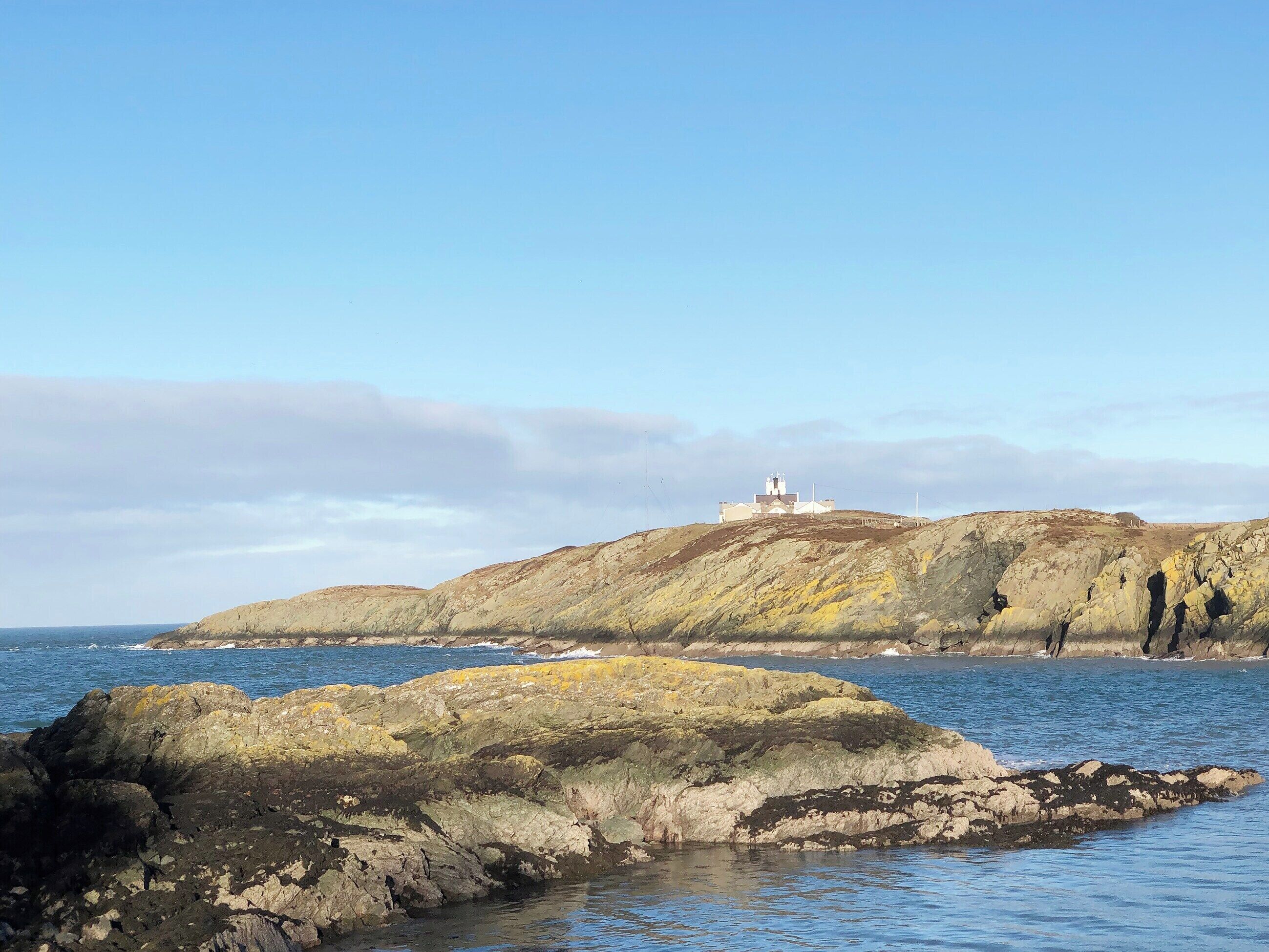 Eine Küstenlandschaft mit felsigem Gelände und einem Leuchtturm auf einem Hügel.