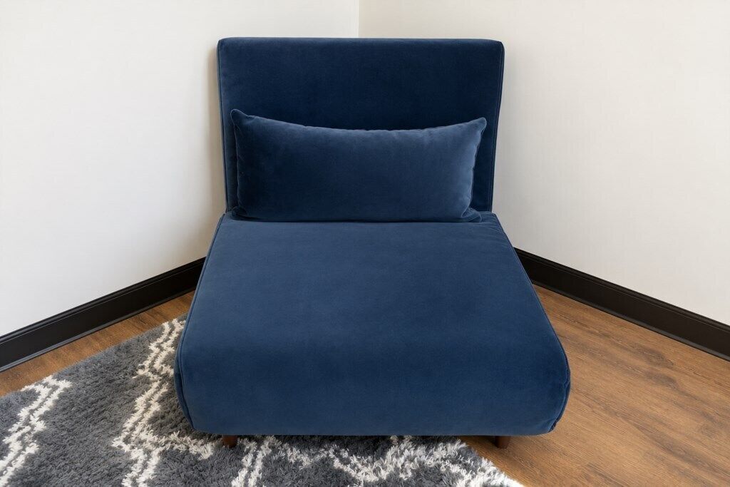A corner sofa with a matching pillow against a white wall, a patterned rug, and wooden flooring.