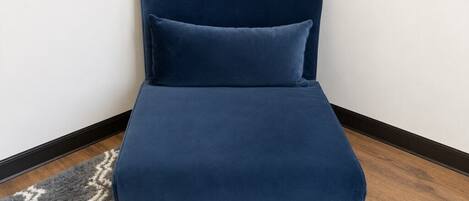 A corner sofa with a matching pillow against a white wall, a patterned rug, and wooden flooring.