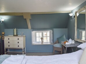 Et soveværelse med seng, kommode, vindue med skodder, stol, spejl og bakke med tesæt.