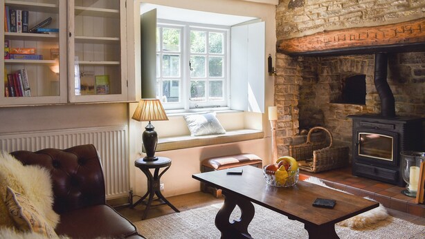 Una sala acogedora con chimenea, una estantería, un ventanal y un sofá de cuero.