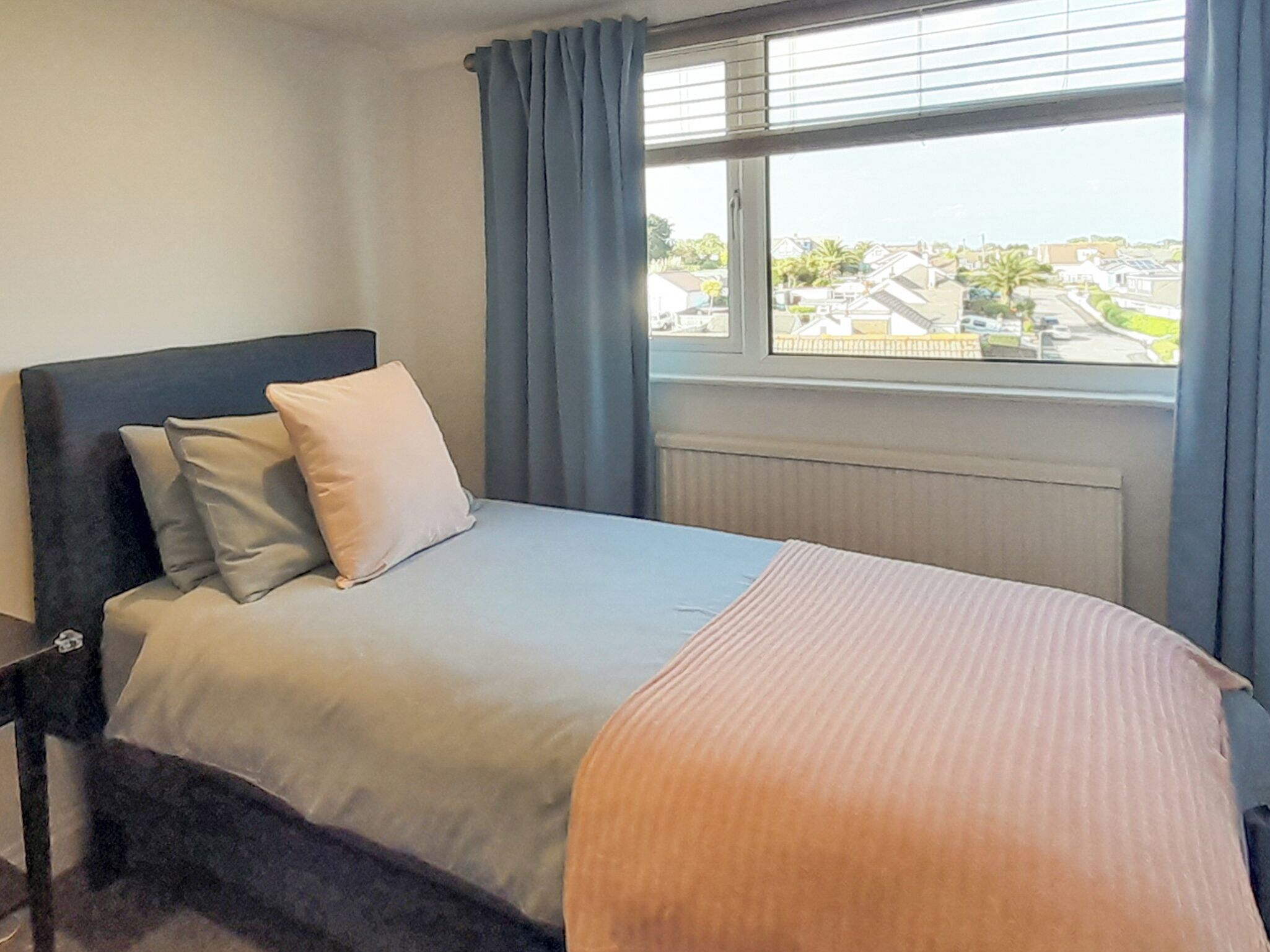 A bedroom with a bed, a window with a view of a residential area, and a radiator.