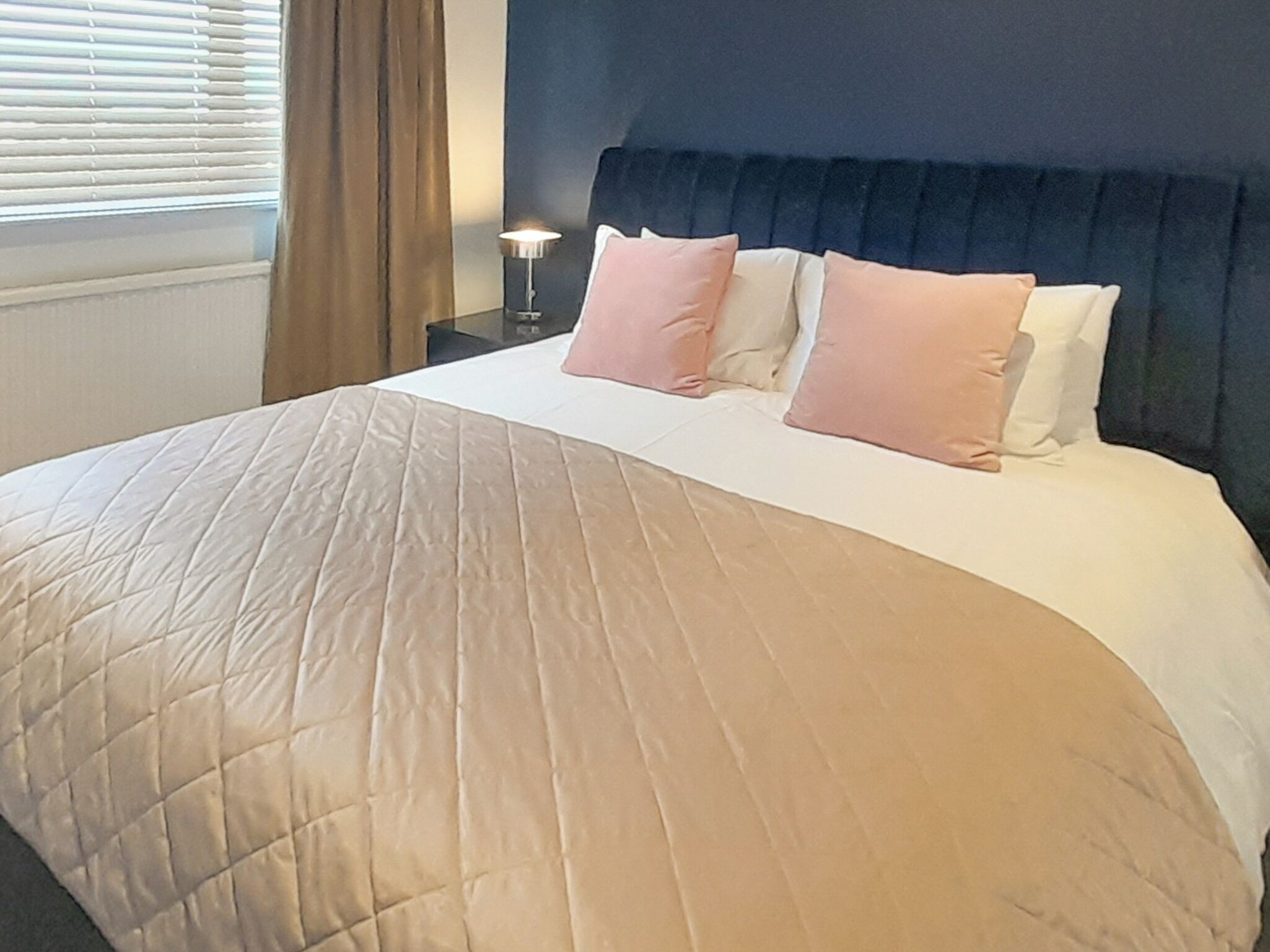 Un letto rifatto con una coperta beige, una testiera scura e due abat-jour.