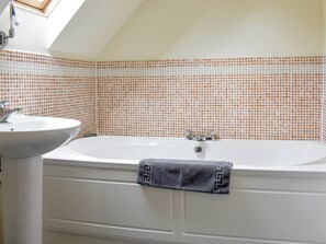 Un baño con una bañera blanca, un lavamanos y una pared con azulejos.