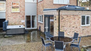 Ein zweistöckiges Backsteingebäude mit einer Terrasse, die einen runden Tisch, Stühle, eine Whirlwanne und eine überdachte Sitzgelegenheit bietet.