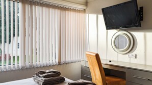 Ein Hotelzimmer mit einem Bett, einem Schreibtisch mit Flachbildfernseher, einem Sessel und einem Spiegel.