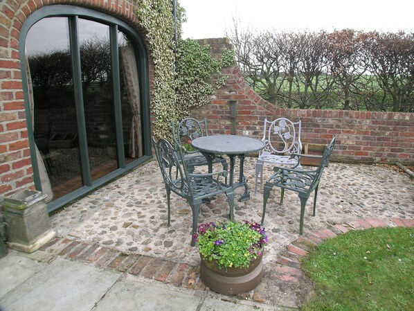 A patio with a round table and four chairs, a potted plant, and a brick wall.