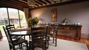 Un comedor con una mesa redonda, sillas de madera y un jarrón con flores amarillas.
