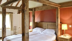 Una cama con dosel, un cabecero de madera, una mesita de noche con lámpara y una ventana con cortinas.