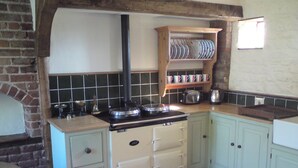 Una cocina con pared de ladrillo, repisa de madera con vajilla, estufa y salpicadero de azulejos.