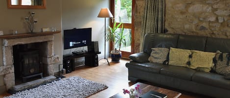 A living room with a stone wall, a fireplace, a sofa, a coffee table with a book and flowers, and a television.