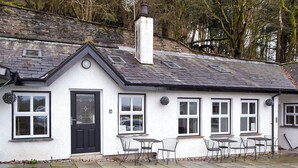 A white cottage with a black door, multiple windows, and a small outdoor seating area with metal chairs. - 1 bedroom accommodation in Clappersgate, near Ambleside (Clappersgate, near Ambleside)
