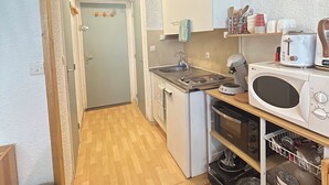 Une cuisine de taille réduite avec un plancher en bois, des armoires blanches, un évier, une cuisinière et un four à micro-ondes.