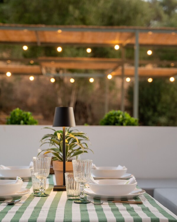 A dining table set with plates, glasses, and cutlery, a lamp, and a potted plant.