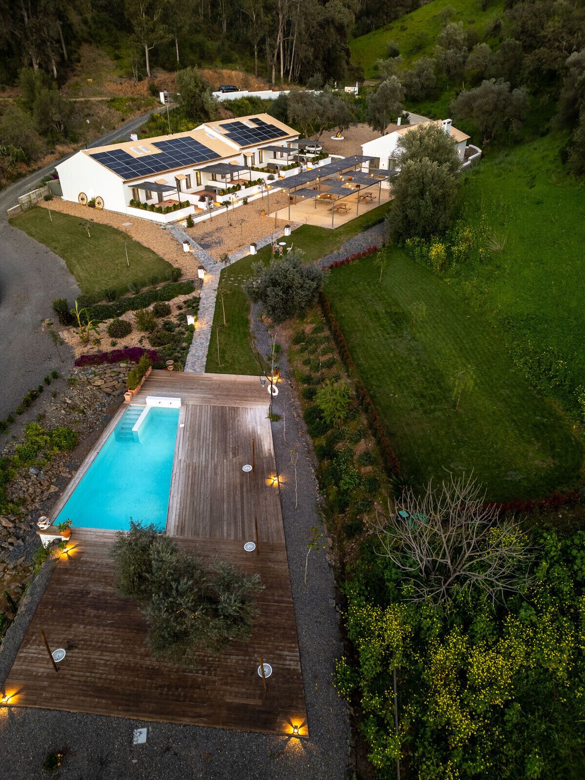 Una casa grande con piscina, rodeada de un jardín cuidado y una terraza de madera.
