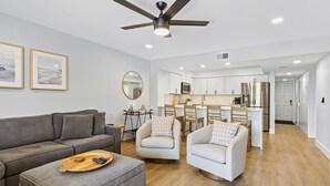 A modern living room with a grey sofa, two armchairs, a wooden coffee table, and a ceiling fan. - Beautiful Fully Renovated Pool View Unit Just A Short Stroll To Beach Access! (Saint Augustine)
