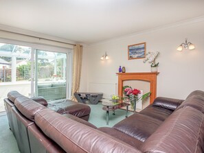 Un salon avec des canapés en cuir, une table basse en verre, une cheminée et une vue sur l’extérieur grâce à une porte vitrée.