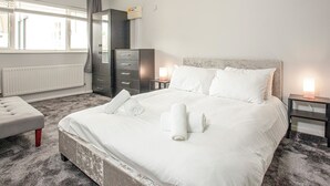 Un dormitorio con cama, cómoda, radiador y ventana con cortinas.